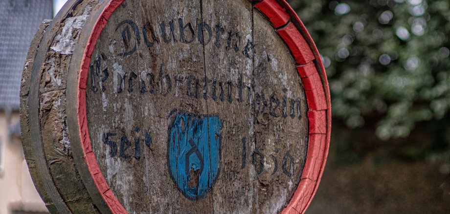 Alter Brunnen im Ortsteil Dauborn, zeigt den Anschnitt eines Fasses mit verwitterter Schrift (nicht lesbar)